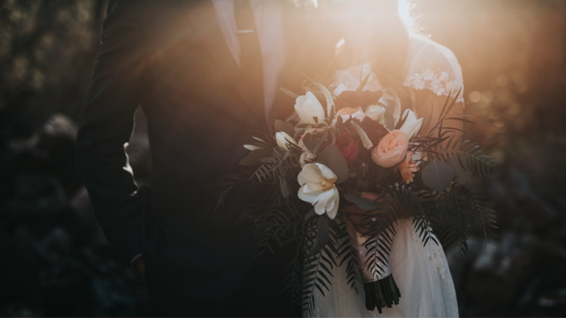 A bride and groom backlit by golden evening light, holding a bouquet